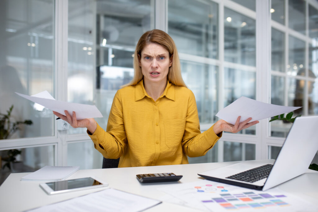 Frustrated loan officer sitting at a desk with paperwork and a laptop, representing the confusion many lenders face when reviewing private flood insurance policies versus NFIP requirements.