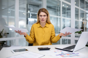 Frustrated loan officer sitting at a desk with paperwork and a laptop, representing the confusion many lenders face when reviewing private flood insurance policies versus NFIP requirements.